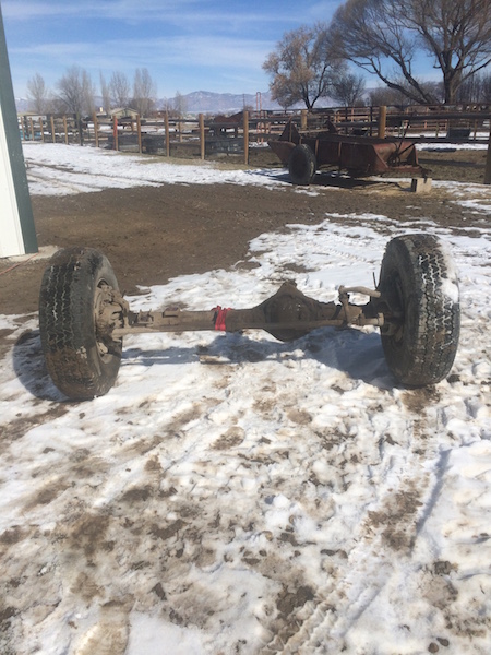 1981 Ford Bronco - A rear axle assembly with two tires is resting on the ground, partially covered in snow and mud. The axle appears to be from an older vehic…
