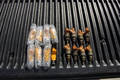 1994 Ford Bronco - A collection of eight fuel injectors, five of which are individually wrapped in plastic, are laid out on a ribbed black surface. The expose…
