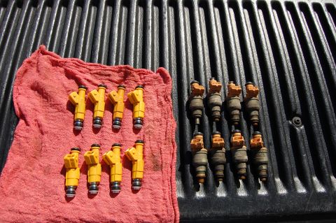 1994 Ford Bronco - A set of eight yellow fuel injectors are laid out on a red cloth, and another set of eight gray and orange fuel injectors are laid out on a…