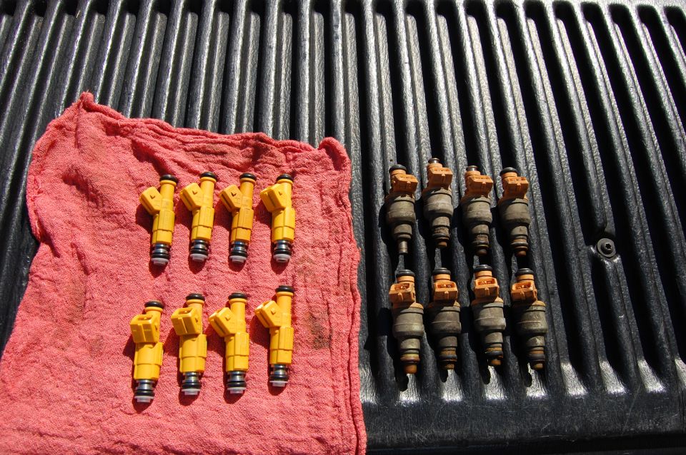 Eight yellow and eight gray/orange fuel injectors on a red cloth and black ribbed surface.