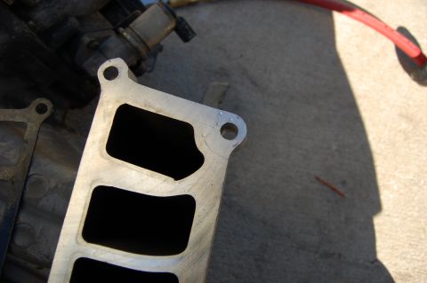 1994 Ford Bronco - A close-up view of an aluminum intake manifold with four rectangular openings. The manifold is resting on a concrete surface with shadows c…