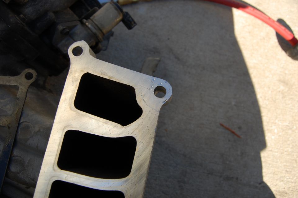 Close-up of an aluminum intake manifold with four openings on a concrete surface.