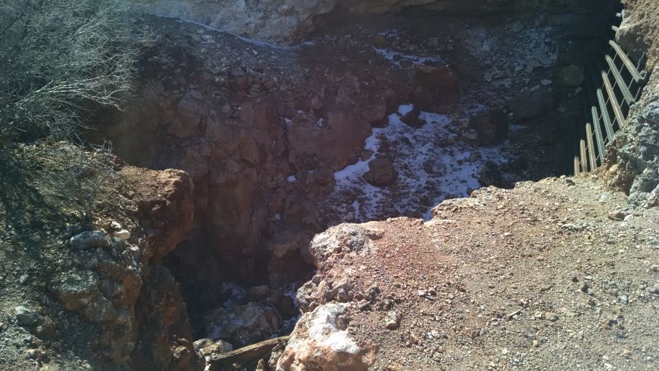 A deep, rocky pit with snow patches and a wooden fence.