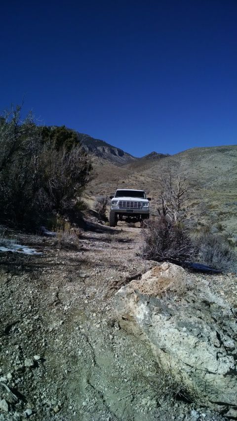 1979 Ford Bronco - A white 1979 Ford Bronco is parked on a rocky, off-road trail in a mountainous, arid landscape under a clear blue sky. The Bronco is lifted…