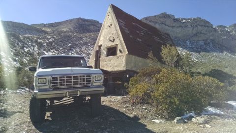 1979 Ford Bronco - A lifted, white 1979 Ford Bronco sits parked on a dirt road in front of a dilapidated A-frame structure in a mountainous, snowy landscape.
