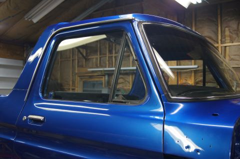 1979 Ford Bronco - Close-up side view of a bright blue pickup truck cab, showing the driver's side door, window frame, and part of the windshield. The vehicle…