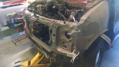 2000 Chevrolet Astro - The front end of a red Chevrolet Astro van is disassembled in a garage setting. The vehicle is on a yellow jack, with the hood and front bu…