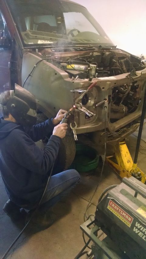 2000 Chevrolet Astro - A person wearing a welding mask is welding the front fender of a vehicle that appears to be a 2000 Chevrolet Astro. A yellow jack stand is…