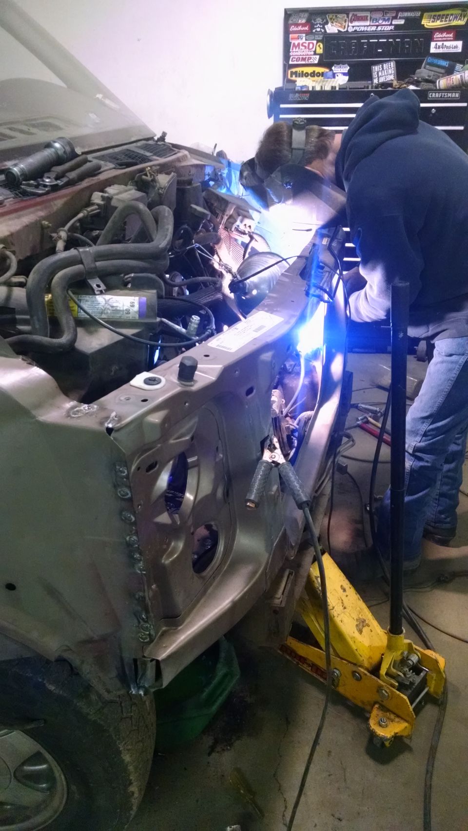 Person welding the inner fender of a vehicle in a garage.