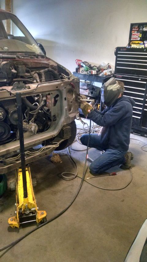 2000 Chevrolet Astro - A person wearing a welding mask and gloves is welding the front end of a vehicle that is supported by a yellow hydraulic jack. The vehicle'…