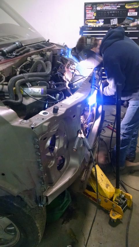 2000 Chevrolet Astro - A person in a welding mask is welding the fender area of a vehicle in a garage. The vehicle's engine bay is visible, along with a yellow hy…