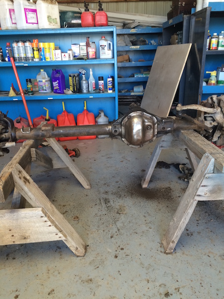 1981 Ford Bronco - A rear axle assembly is supported by wooden sawhorses in a garage setting. Shelving units filled with various fluids and containers are vis…