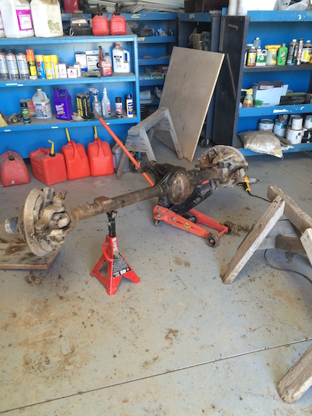 1981 Ford Bronco - A disassembled rear axle assembly is supported by red jack stands in a garage setting. Shelves stocked with various automotive fluids and c…