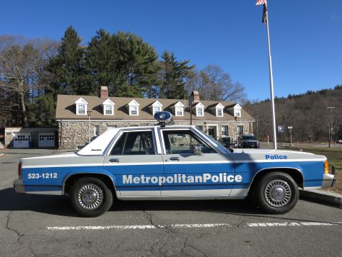 1991 Ford LTD Crown Victoria - Photo of a blue and white Metropolitan Police Crown Victoria parked before a stone building.