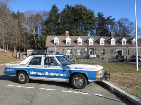 1991 Ford LTD Crown Victoria - Photo of a blue and white Metropolitan Police Crown Victoria parked before a stone building.