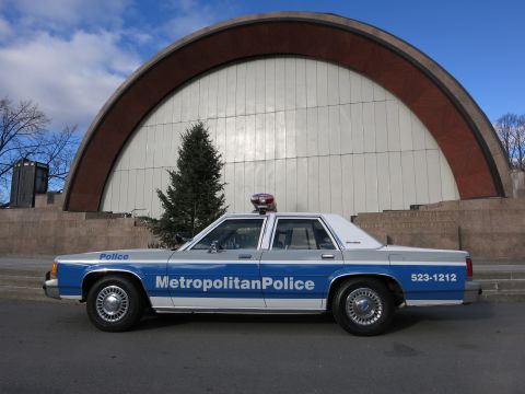 1991 Ford LTD Crown Victoria - Photo of a blue and white Metropolitan Police Crown Victoria parked at an arched bandshell.