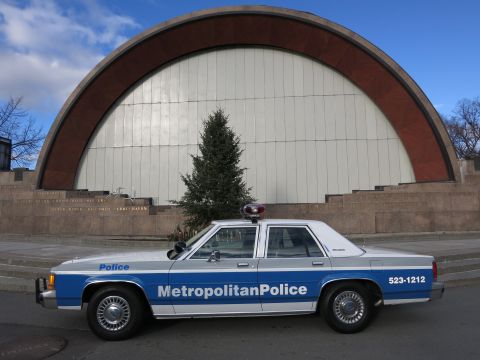 1991 Ford LTD Crown Victoria - A 1991 Ford Crown Victoria police car is parked in front of a modern building with a large arched facade.