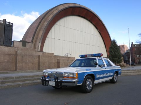 1991 Ford LTD Crown Victoria - Photo of a blue and white Metropolitan Police Crown Victoria cruiser parked near a domed bandshell, not a technical document.
