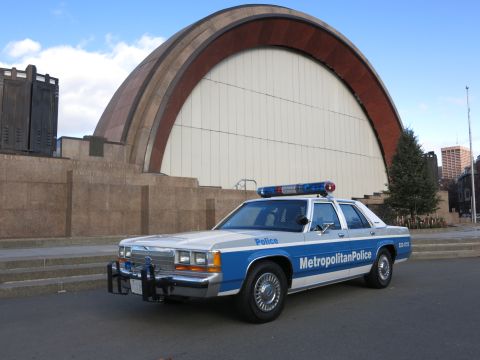 1991 Ford LTD Crown Victoria - Photo of a Metropolitan Police Crown Victoria police cruiser in front of a bandshell, not a technical document.