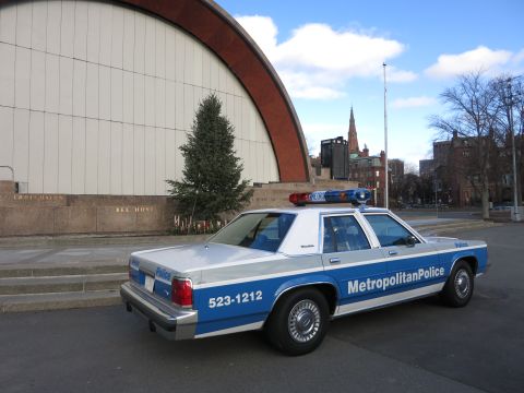 1991 Ford LTD Crown Victoria - Photo of the rear of a Metropolitan Police Crown Victoria cruiser near a park bandshell, not a technical document.