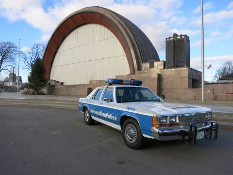 1991 Ford LTD Crown Victoria - Photo of a Metropolitan Police Crown Victoria cruiser on pavement near a park bandshell, not a technical document.