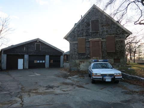 1991 Ford LTD Crown Victoria - Photo of a police Crown Victoria cruiser parked beside an abandoned shingled house, not a technical document.