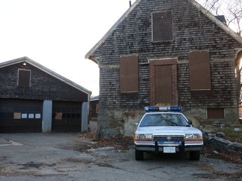 1991 Ford LTD Crown Victoria - Photo of a police Crown Victoria cruiser parked at a boarded-up house with a barn nearby, not a technical document.