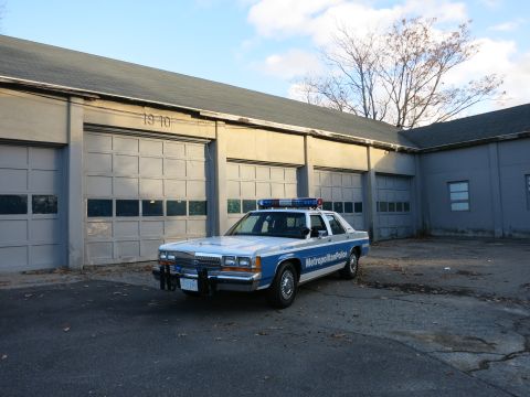 1991 Ford LTD Crown Victoria - Photo of a Metropolitan Police Crown Victoria cruiser at front quarter angle by garage bays, not a technical document.