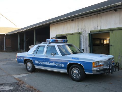 1991 Ford LTD Crown Victoria - Photo of a Metropolitan Police Crown Victoria cruiser parked beside a weathered barn, not a technical document.