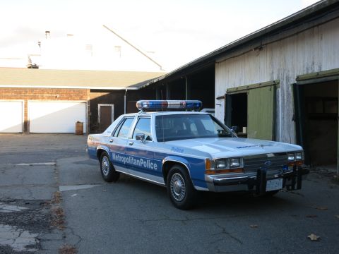 1991 Ford LTD Crown Victoria - Photo of a Metropolitan Police Crown Victoria cruiser parked near old barn buildings, not a technical document.
