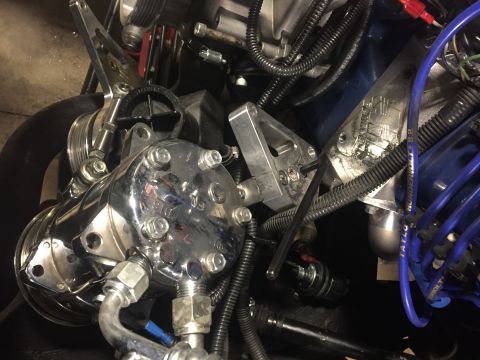 1982 Ford Bronco - A close-up view of a chrome air conditioning compressor mounted on a vehicle engine. The compressor has multiple bolts and fittings, with v…
