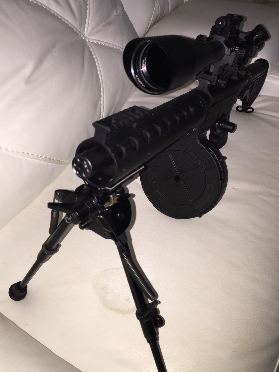 Black rifle with scope and bipod on white cushion.