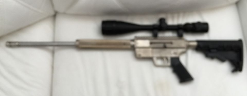 Blurry image of a rifle with a scope on a white background.
