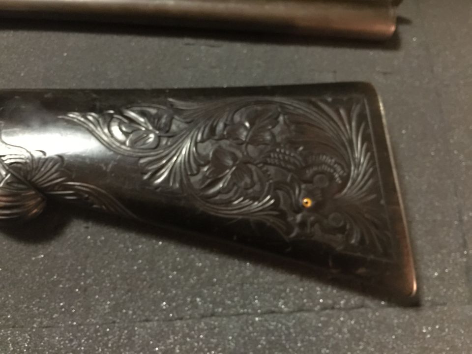 Close-up of engraved floral pattern on a dark wooden firearm stock.