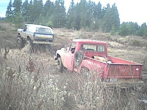 1978 Ford Bronco - A red pickup truck tows a stuck 1978 Ford Bronco out of a muddy field.