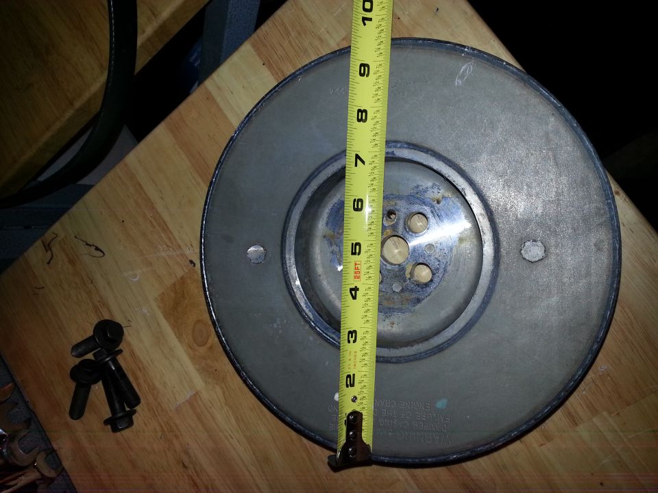Grey circular automotive part with a yellow measuring tape and bolts on a wooden table.