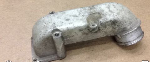 1994 Ford Bronco - This is a close-up, angled shot of a used, silver-colored metal intake manifold part. The part shows signs of wear and some discoloration,…