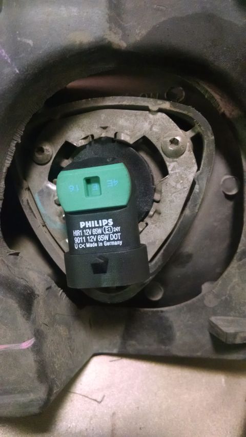 2000 Chevrolet Astro - A close-up view of a Philips HIR1 12V 65W headlight bulb installed in a vehicle's headlight housing. The bulb is black and green with white…