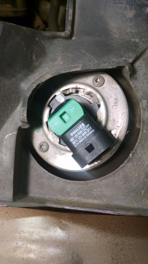 2000 Chevrolet Astro - A close-up view of a Philips HIR1 headlight bulb installed in a vehicle's headlight housing. The bulb is black and green and has text indic…