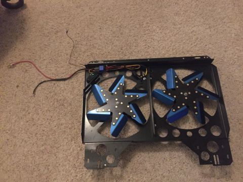 1982 Ford Bronco - A black metal shroud holds two electric cooling fans with blue blades. Wires and a blue relay are visible on the shroud.