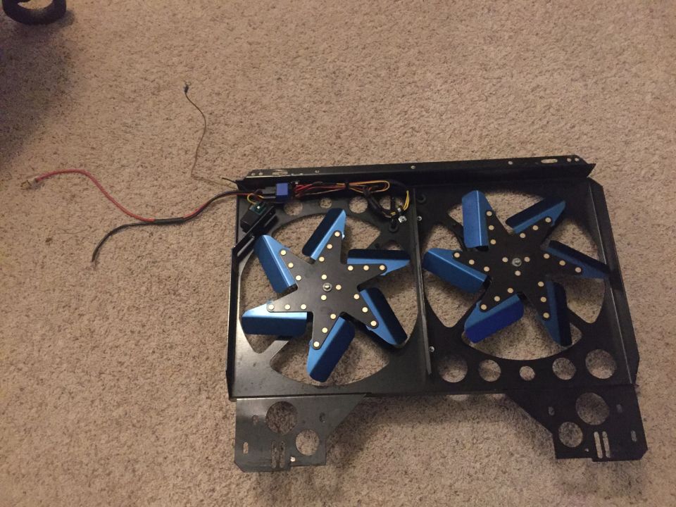Black shroud with two blue electric cooling fans and wiring.