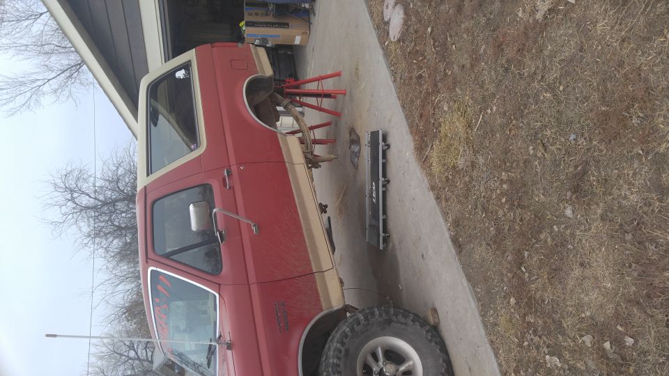 Red and tan Ford Bronco with front wheel removed, on jack stands, with creeper nearby.