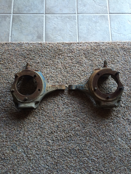 1981 Ford Bronco - Two rusty metal automotive parts, possibly steering knuckles, are shown on a carpeted surface. Each part has a circular opening and a stamp…