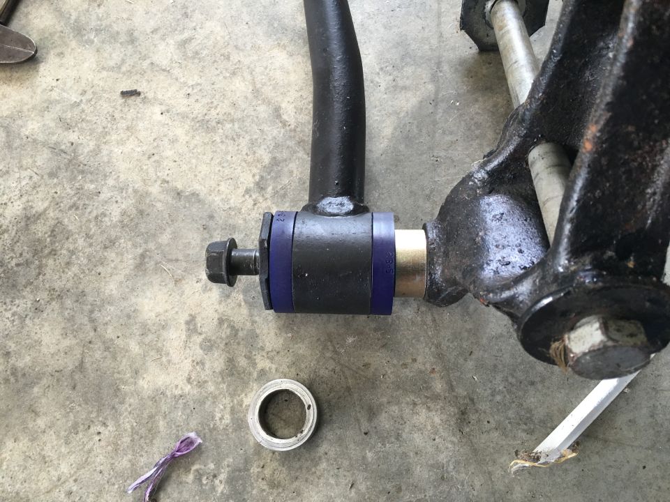 Close-up of sway bar end link with blue polyurethane bushing and bolt on concrete.