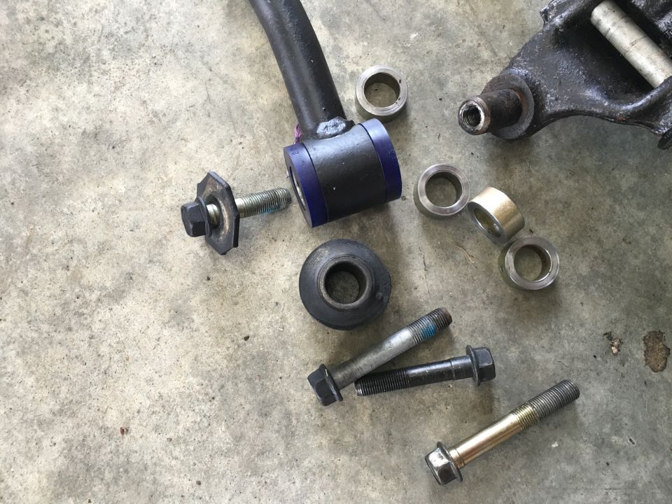 Car suspension parts including bolts, bushings, and a control arm on concrete.