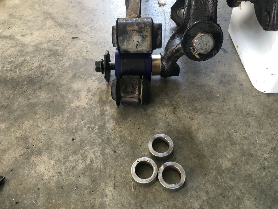 Vehicle suspension components with blue bushing and three metal rings on concrete.