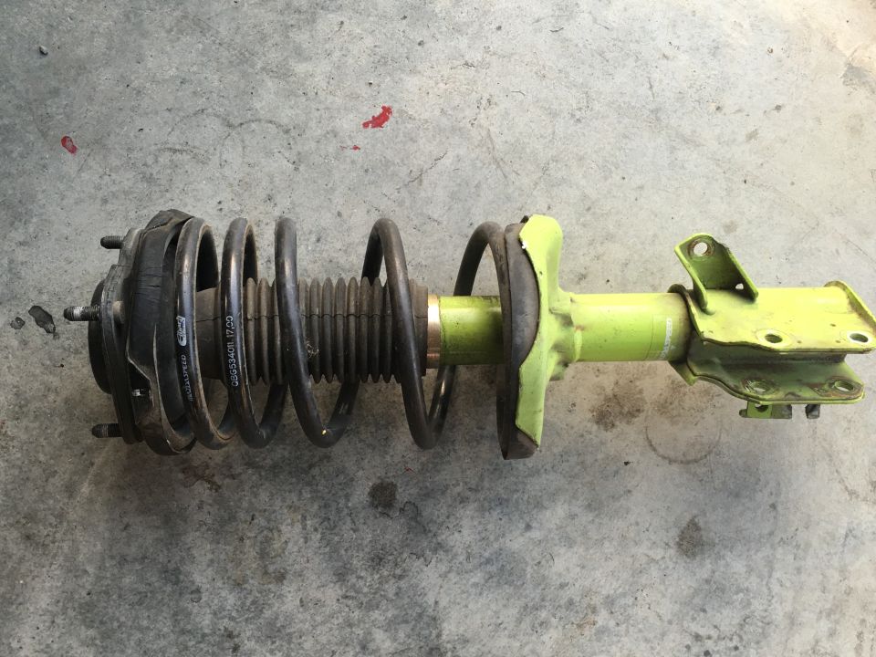 Front strut assembly with yellow shock body and black coil spring on concrete.