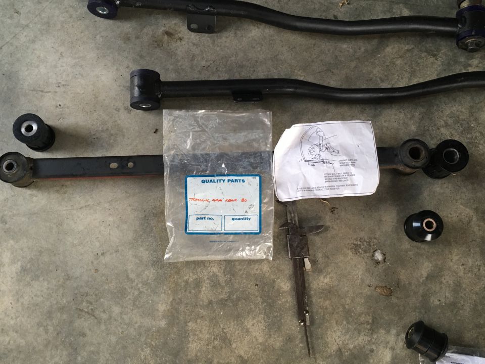 Suspension control arms and bushings on a concrete surface with a parts bag and diagram.