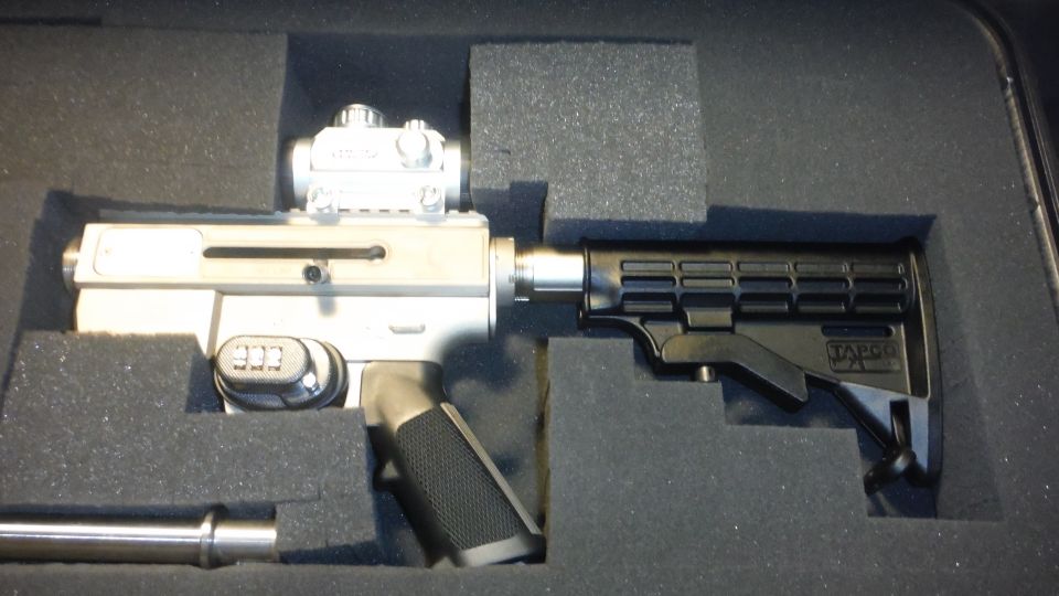 Silver firearm with black stock and red dot sight in a foam case
