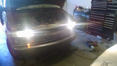2000 Chevrolet Astro - The front of a Chevrolet Astro van with its hood open and headlights illuminated. The vehicle is in a garage setting with tool chests and o…